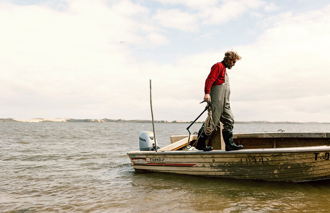 Fisherman walks along edge of his boat on the Coorong