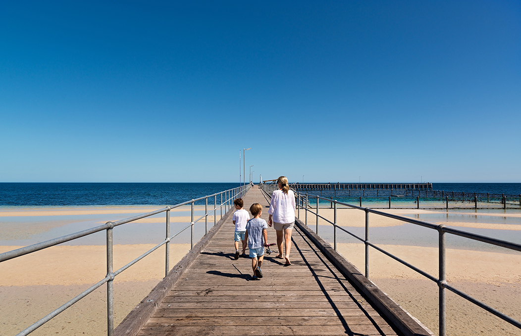 A family walking along the Moonta Bay jetty towards the sea.