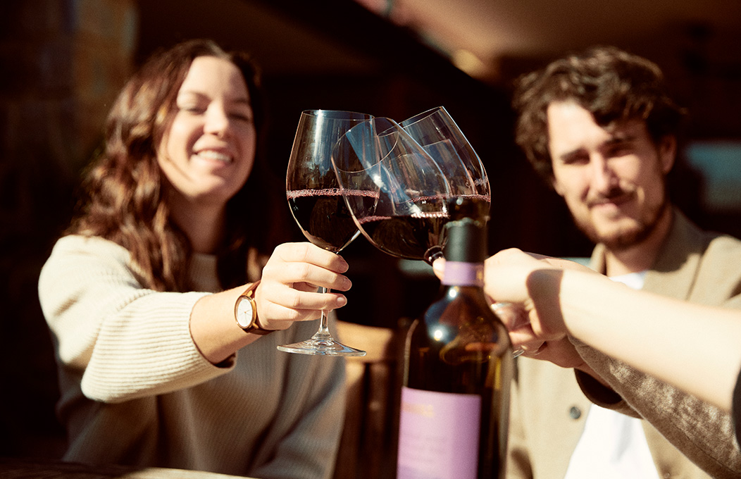 A group on friends in the blur cheering up with the focus of the image being on the glasses they hold in hands in the center.