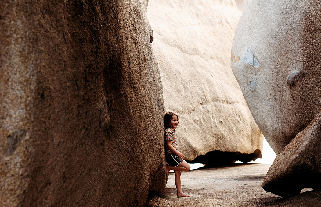 a girl standing between two large granite like boulders