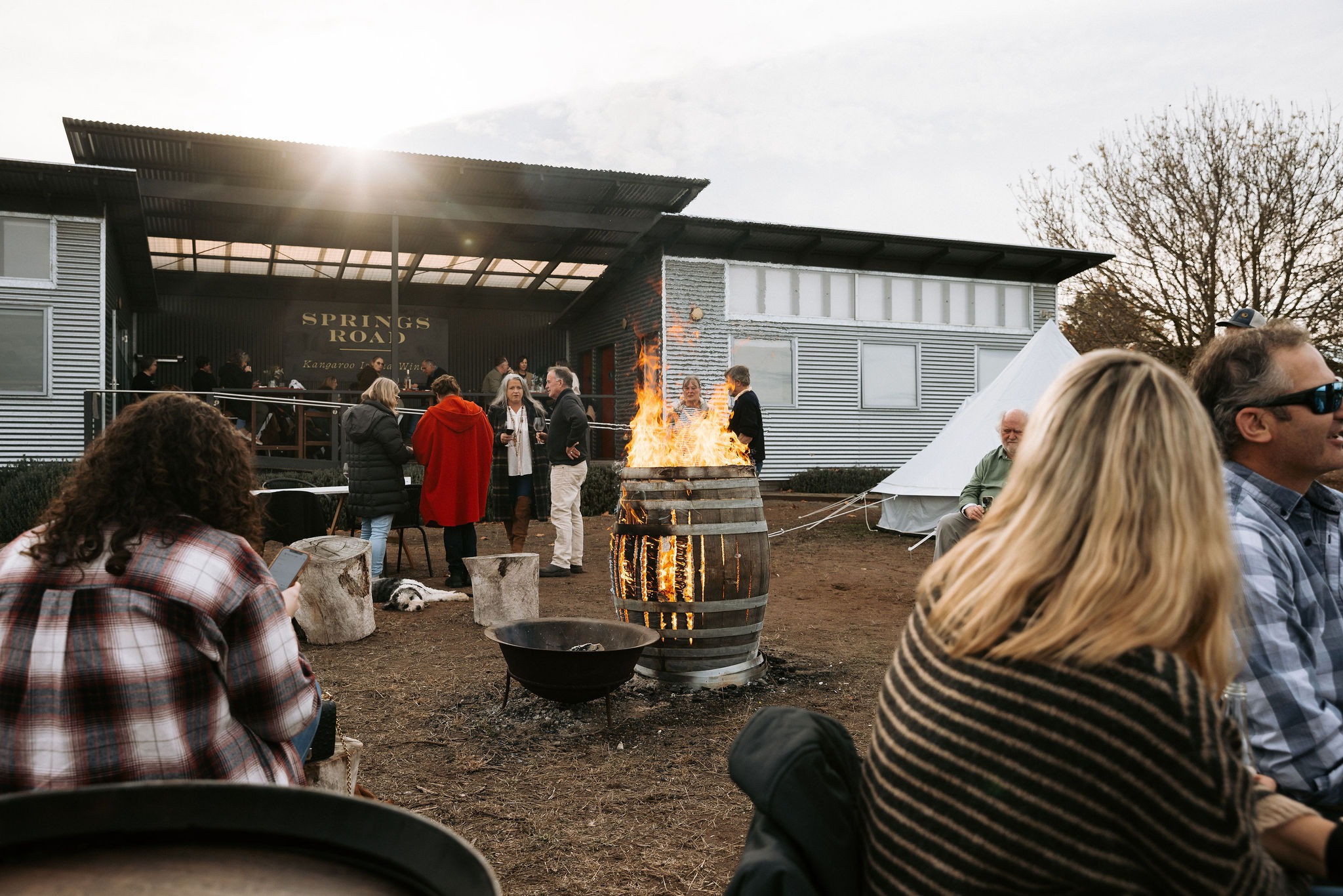 A wine barrel on fire in the middle of a group of people enjoying glasses of wine