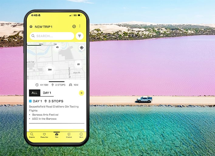 trip planner screen mock-up of the Explore South Australia app over a roadtrip image background showing a 4WD driving between clear blue waters and a bright pink lake.