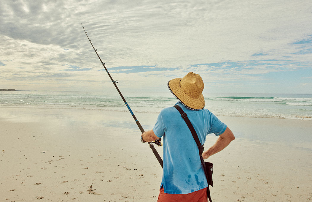 A man standing in the sand fishing in Vivonne Bay Beach