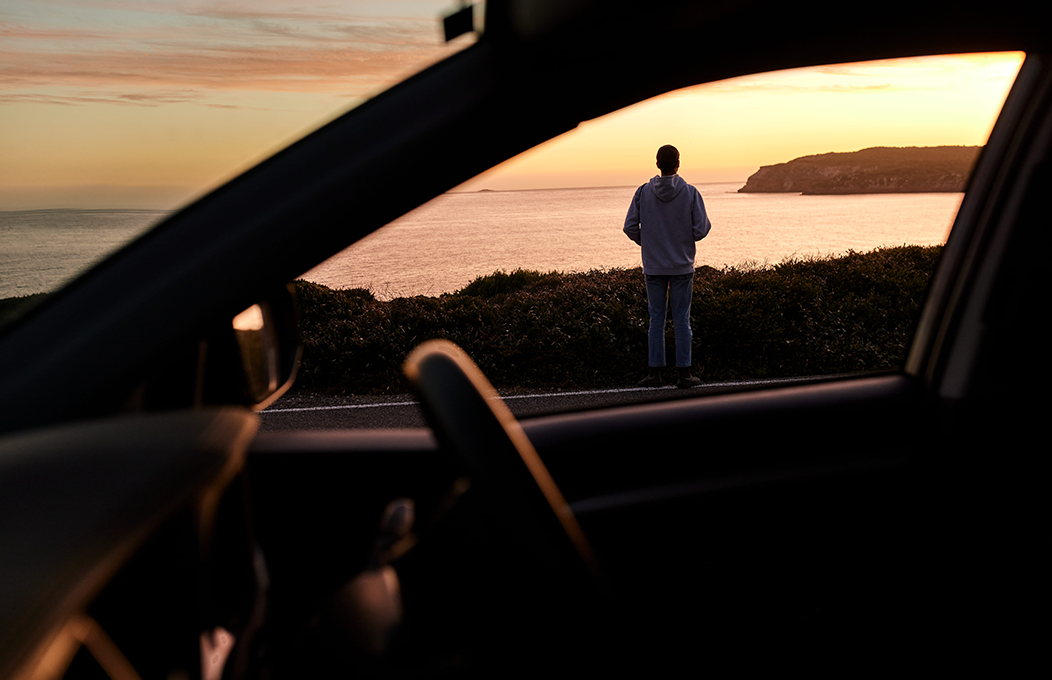 A male overlooking the ocean with a car in the forefront
