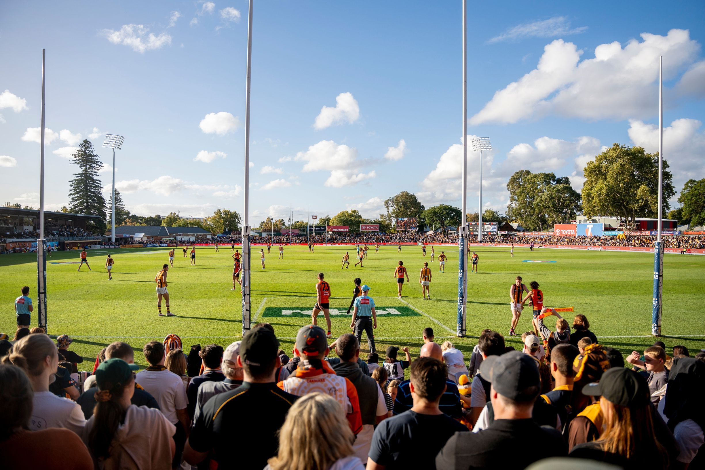 AFL Gather Round spectators watching an Australian football round of the tournament at an outdoor stadium on a sunny day.