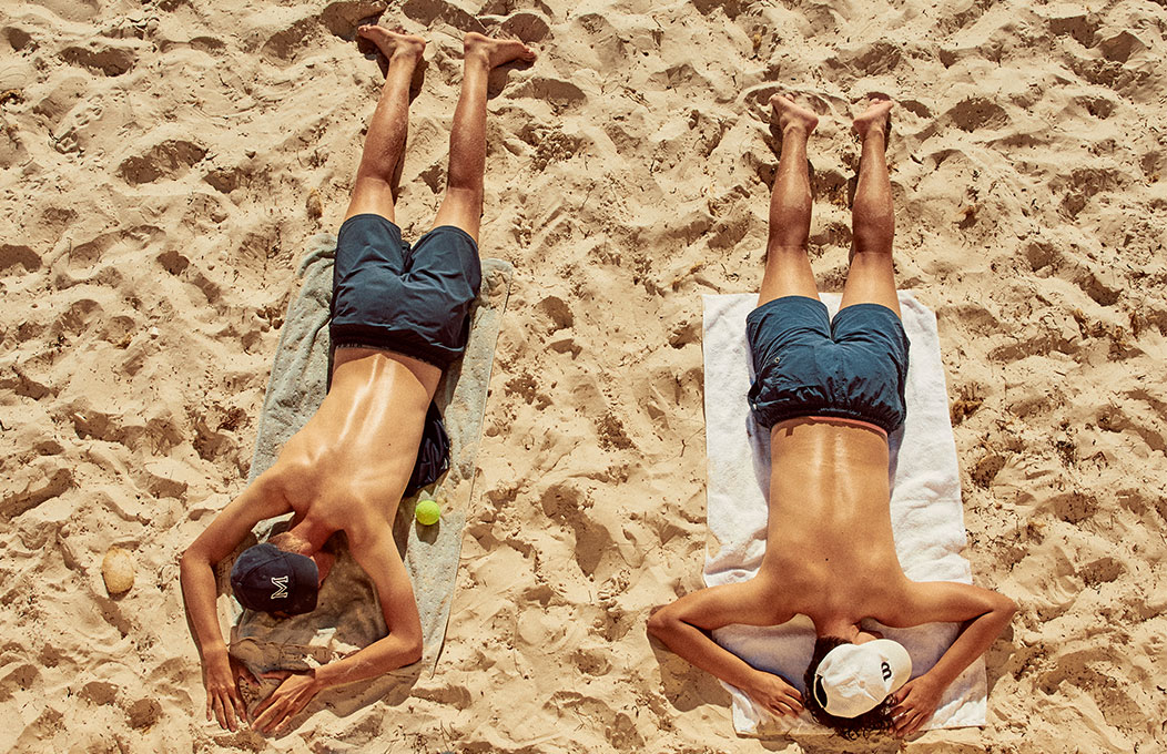 A bird's eye-view of two people laying on their towels on the sand at Henley Beach 