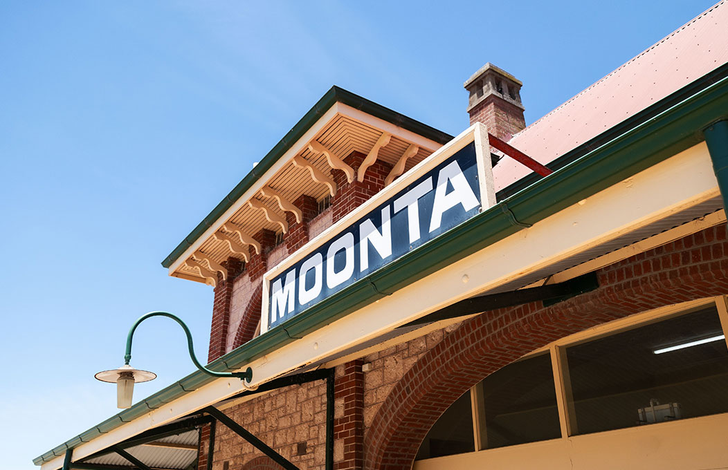 Historic brick building with a green-trimmed roof and a large sign reading ‘MOONTA’ under a clear blue sky.