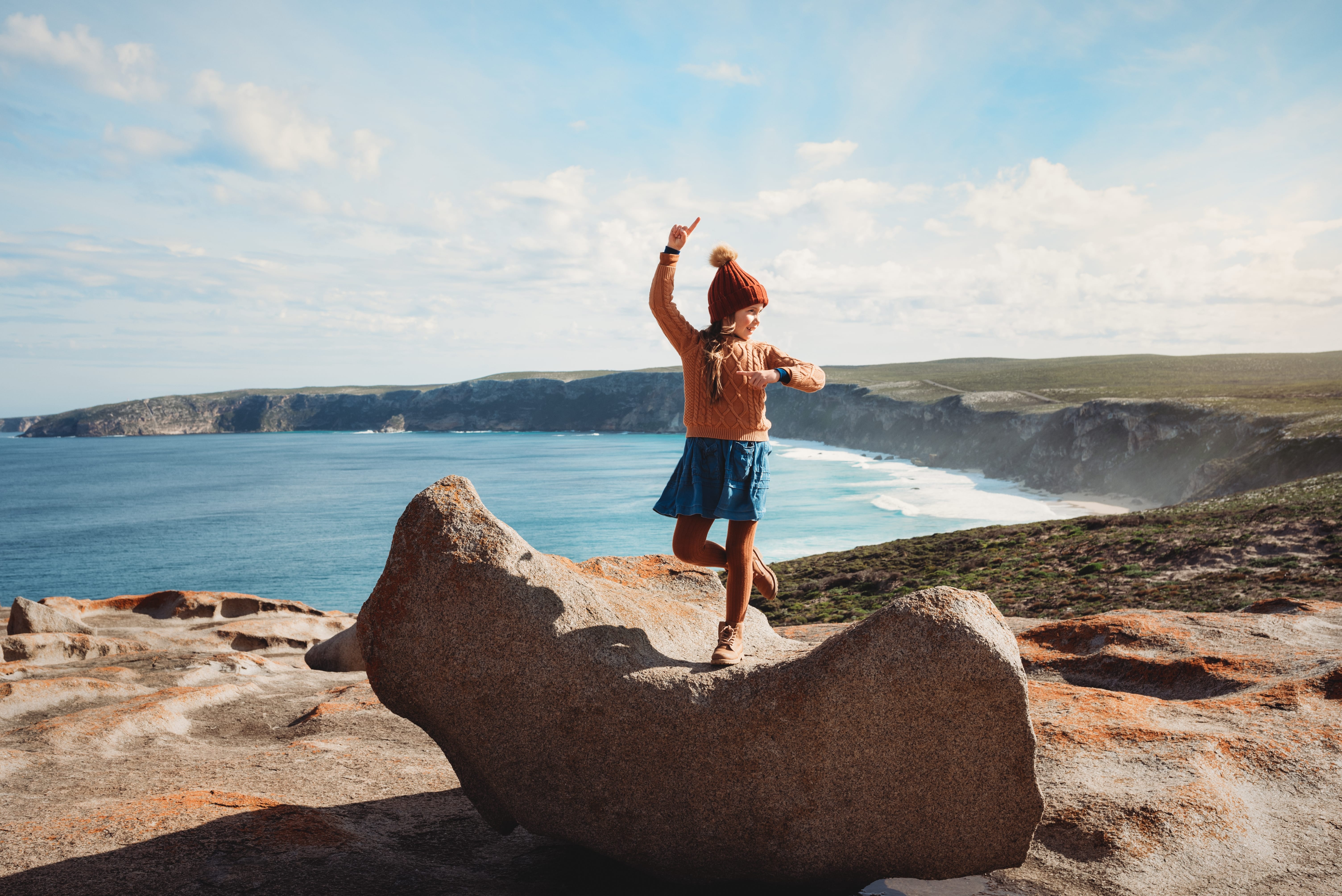 A girl posing on one of the curve shaped Remarkable rocks in front of the stunning coastline of the Flinders Chase national park