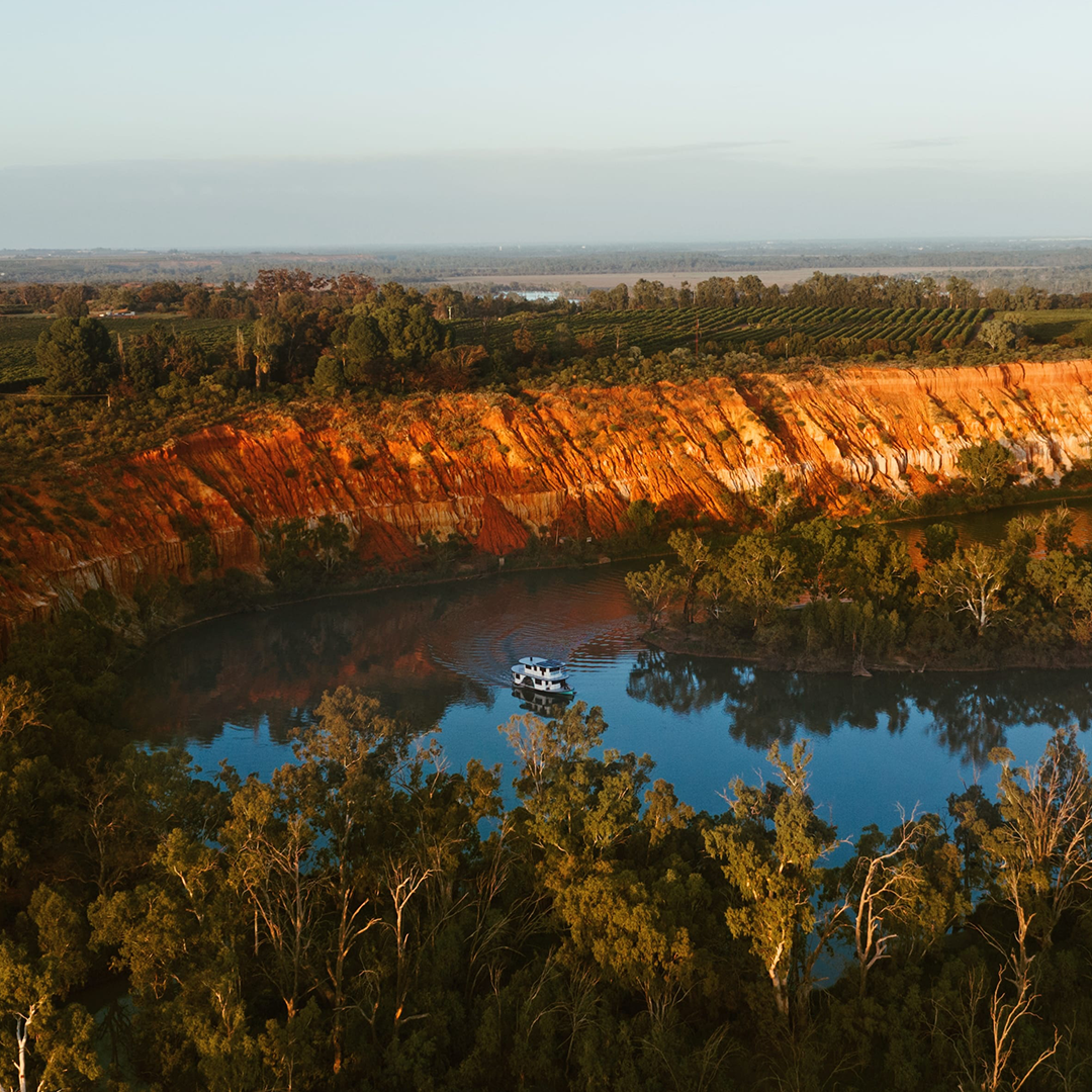 a houseboat floats on calm water, with orange cliffs in the background