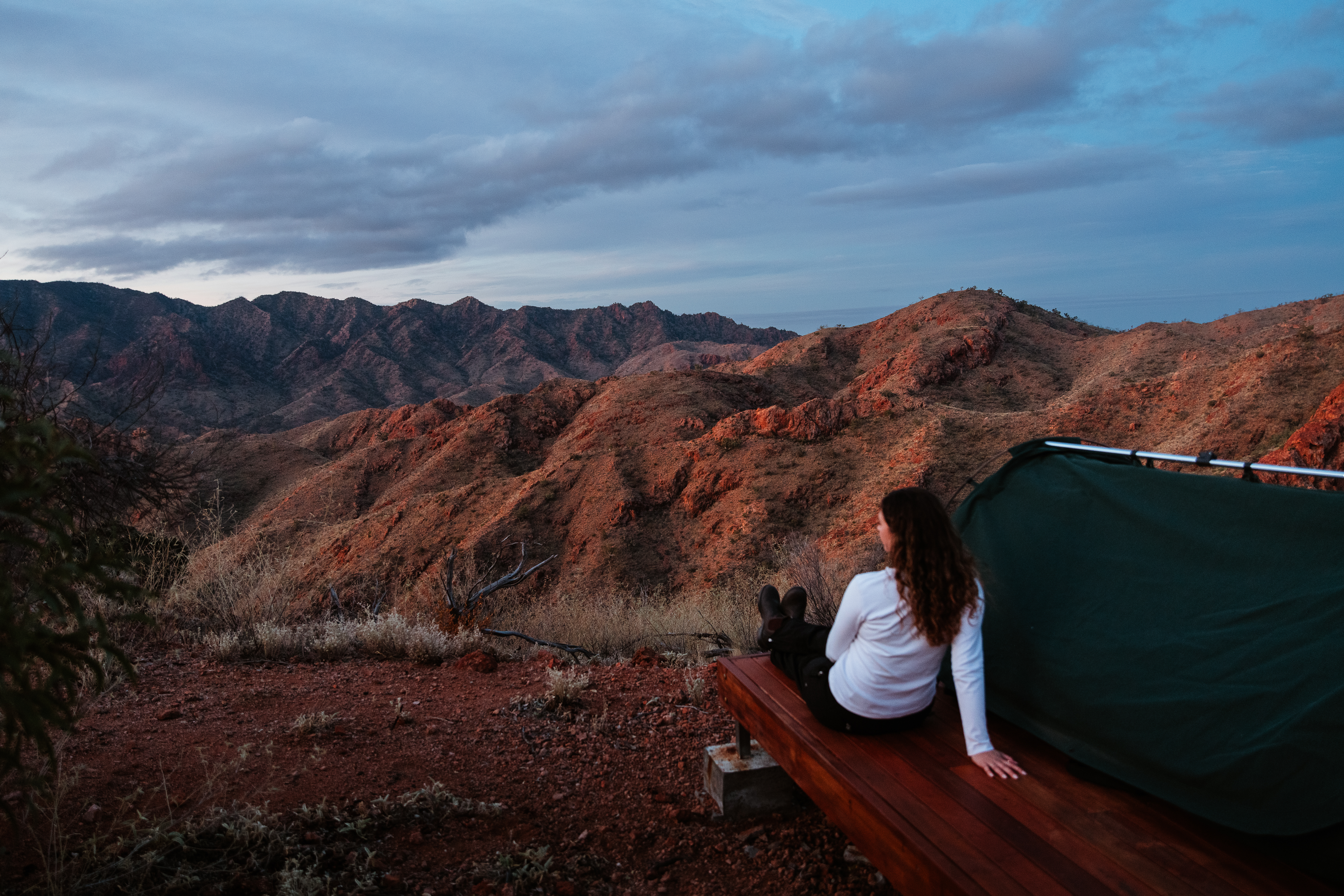 person leaning next to swag looking out at a mountain landscape 