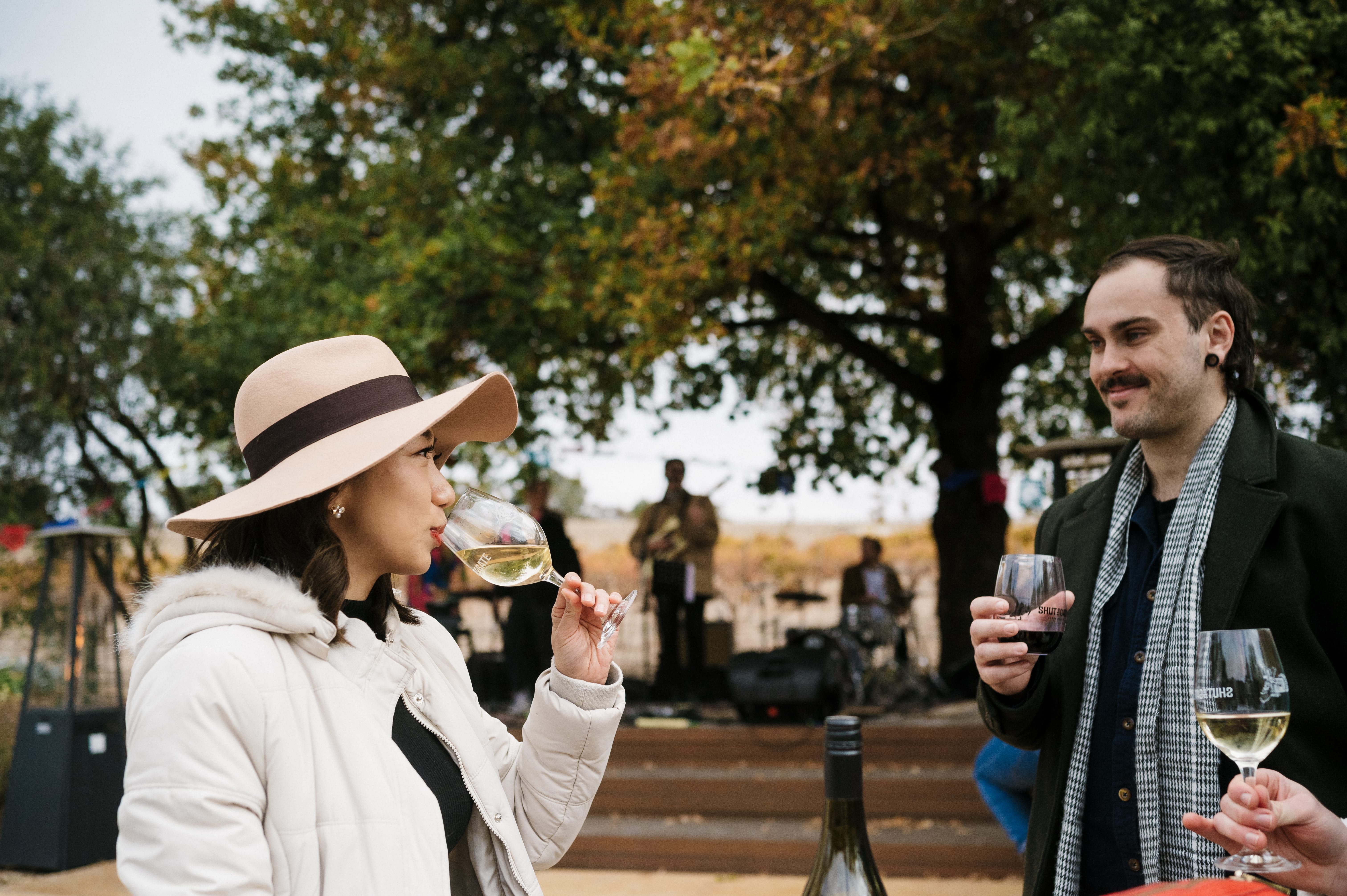 A women drinking a glass of white wine looking at a aman and someone else in the corner of the photo holding glasses of white wine.