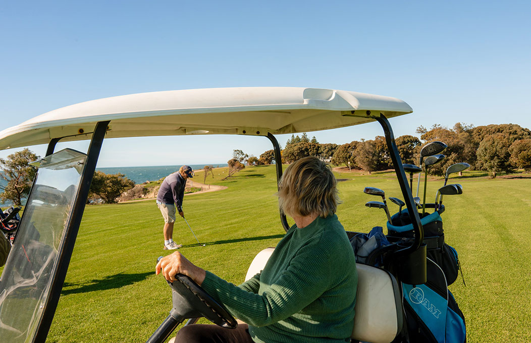 Golf cart on a green fairway overlooking the ocean as a golfer lines up a shot.