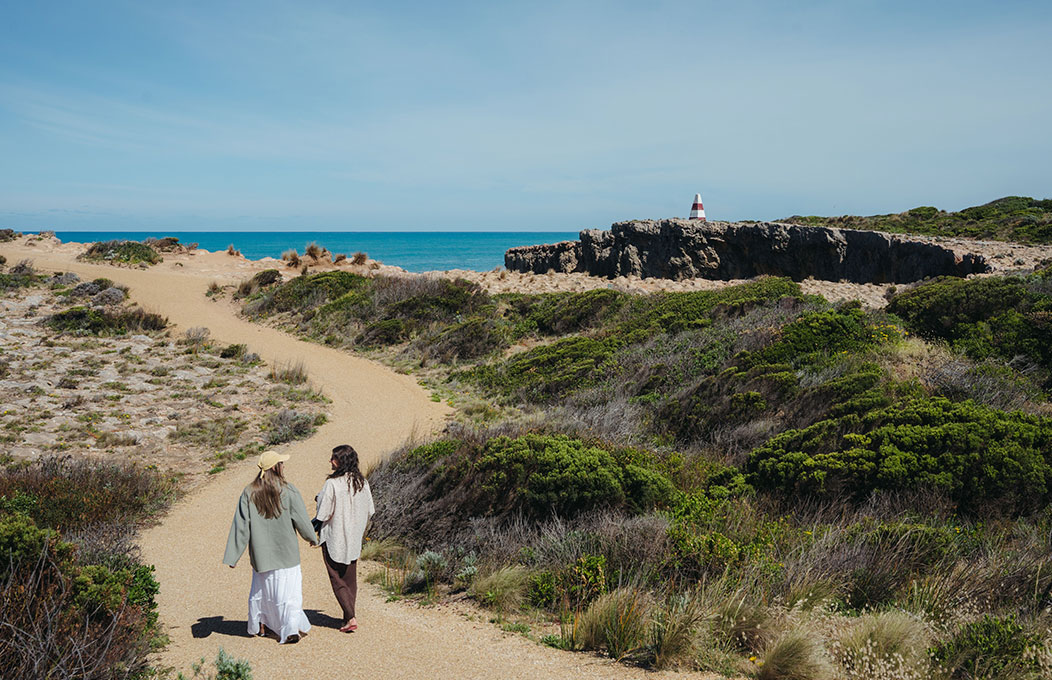 Two people walk the track towards the Obelisk, with the bright blue water in the distance
