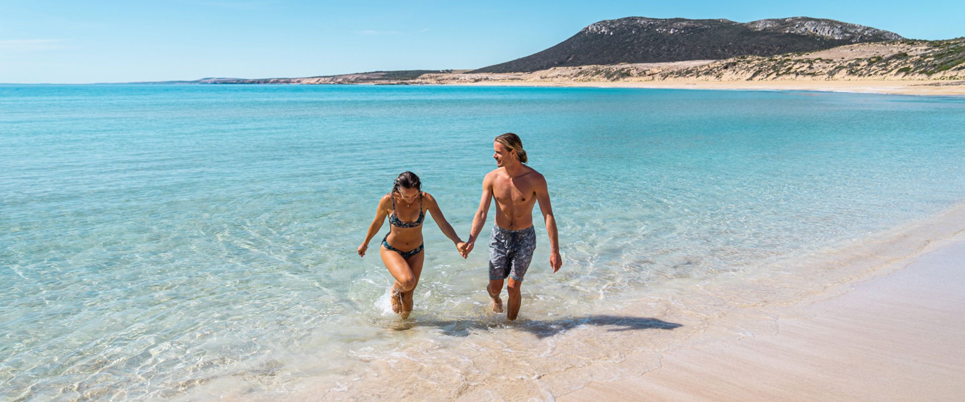 Two young people on a beach with white sand and bright blue water