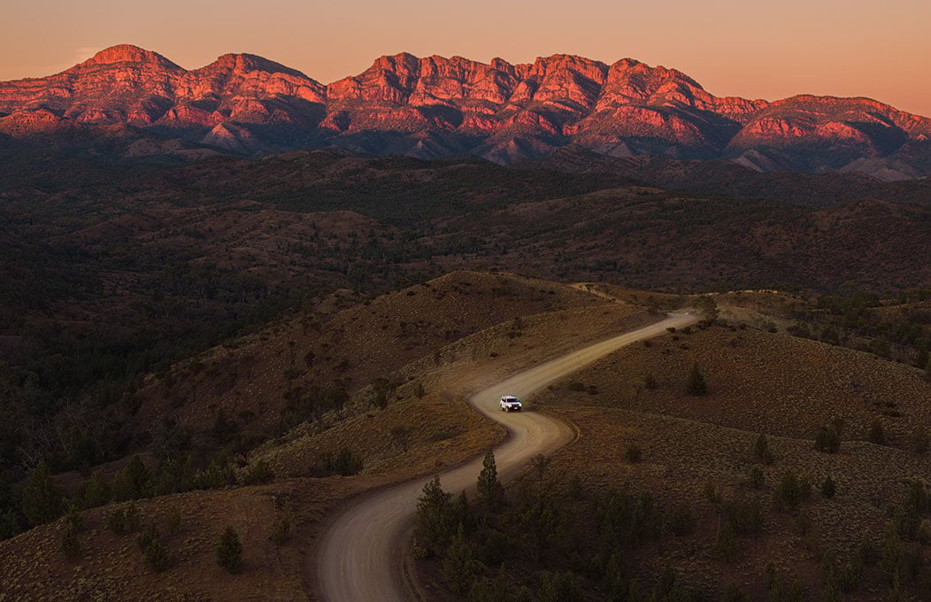 A winding road over a ridgetop at sunset with mountains in the background