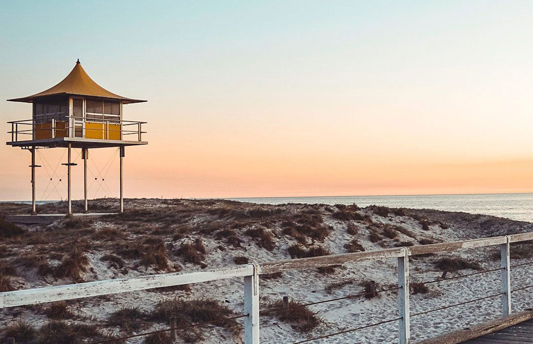 The yellow lifeguard tower stands tall over the sand of Semaphore, as the sun turns the sky a tangerine