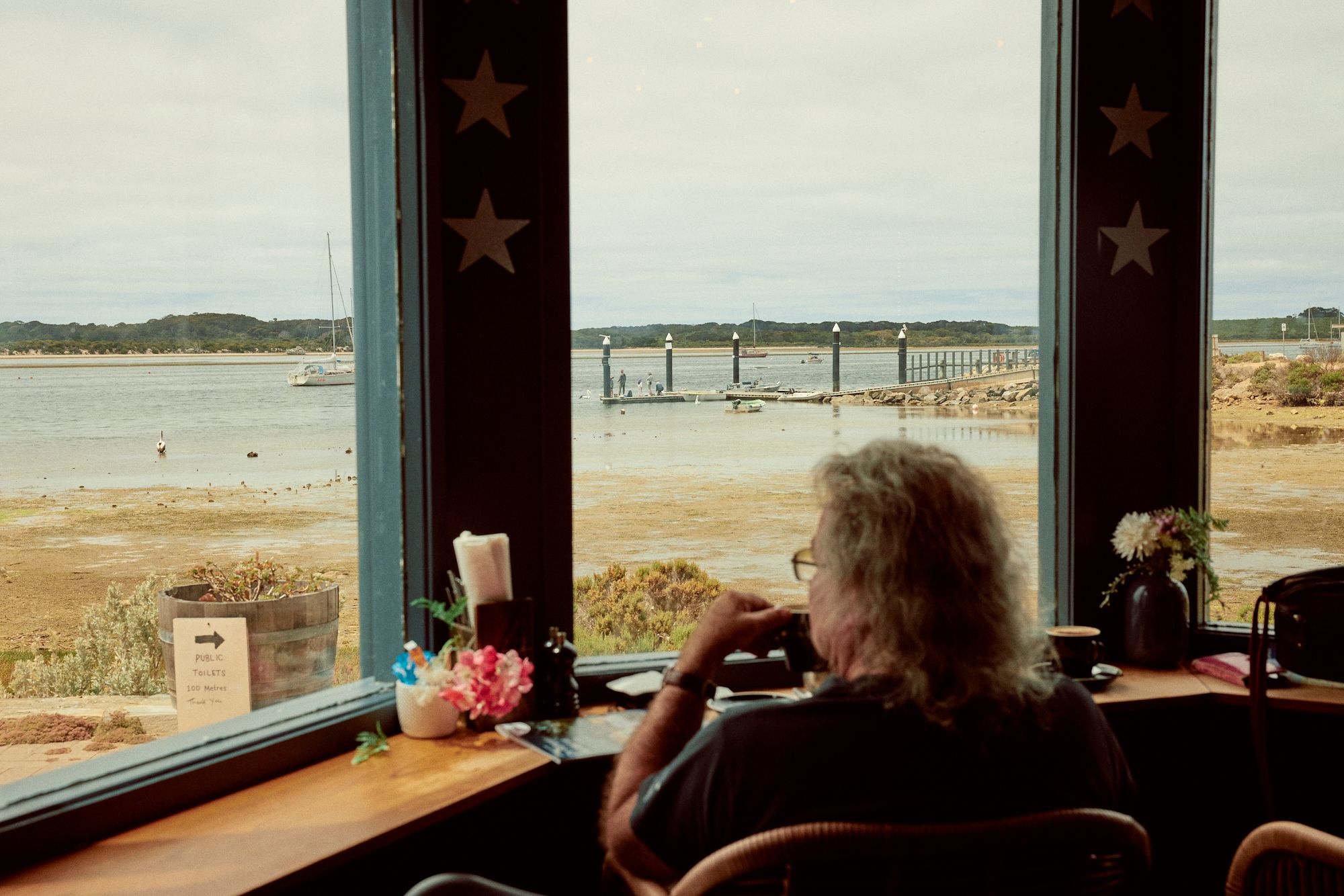 A visitor sipping his coffee cup in front of the American River coastal view through the windows of the KI Oysters