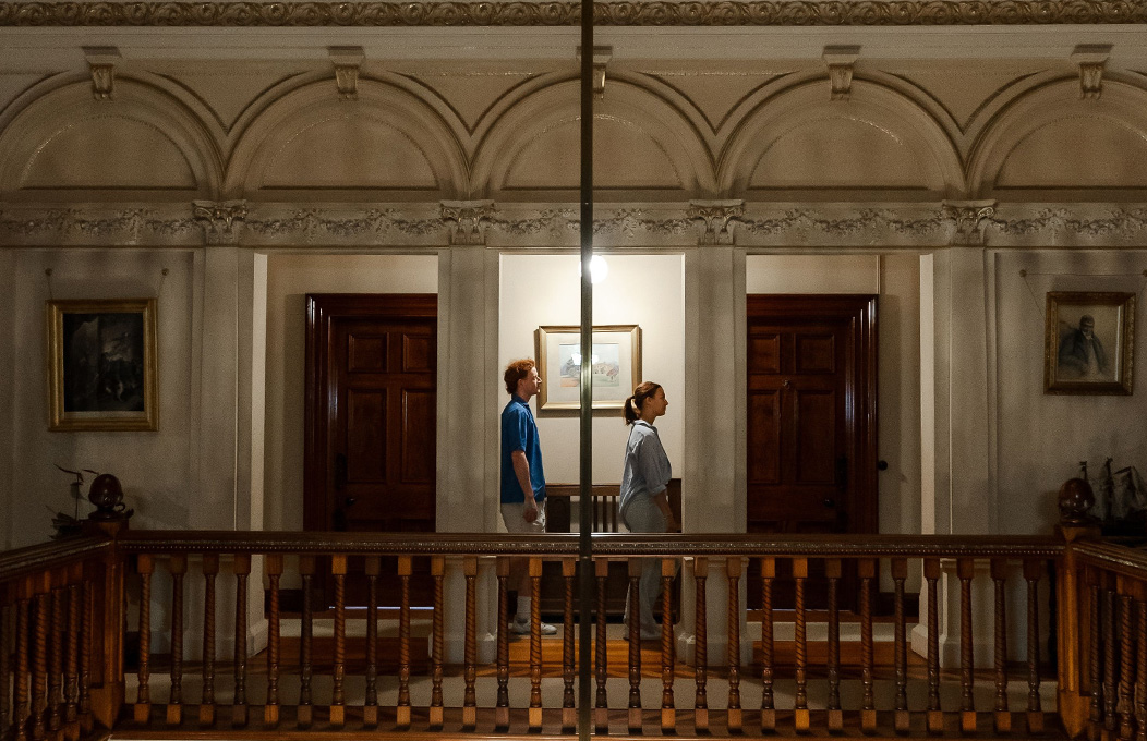 2 people seem to be following a tour, standing in the middle of the upper deck of the Martindale Hall inside, in between two wodden doors.